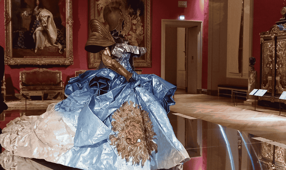 La théâtralité de la silhouette baroque louis-quatorzienne aux notes punk rock a trouvé un parfait écrin dans cette salle où la robe qui arbore le motif du soleil fait écho au portrait du Roi Soleil, en arrière-plan. Collection Dior Haute Couture AH 2006-07 : robe en organza de soie brodé et peint, bras-armure et casque - Photo © Stéphanie Bui.