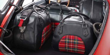 Set de bagages Coventry en cuir pleine fleur et drap de laine tartan, assortis à l’habitacle. La sangle rappelle le harnais de compétition.